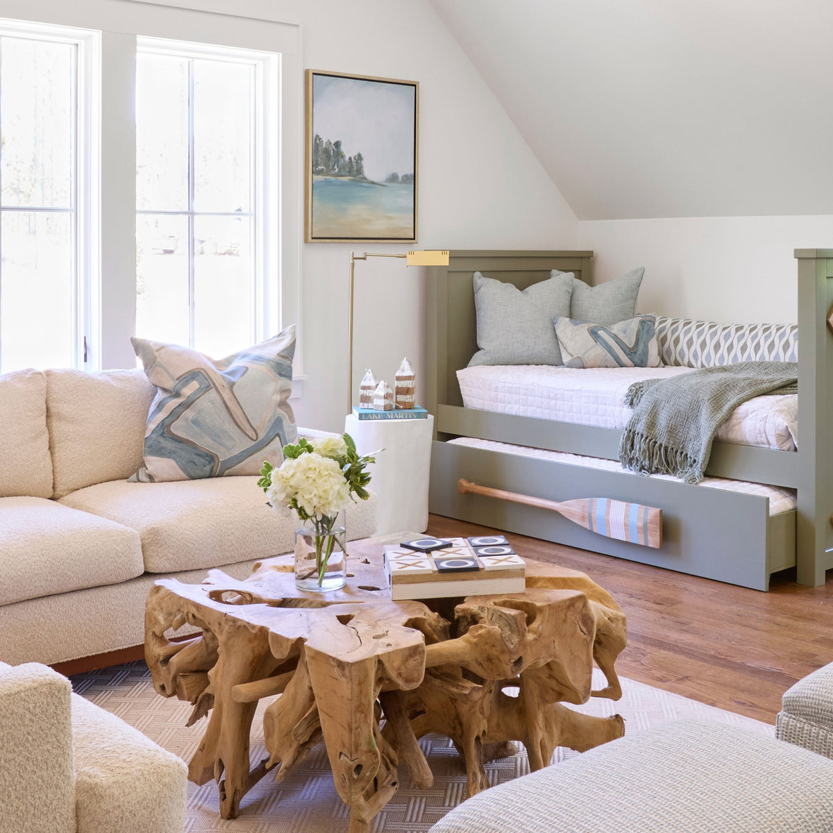 A living room styled with abstract blue and ivory patterned pillows on a cream sectional and daybed, alongside a teak root coffee table and lake house decor.