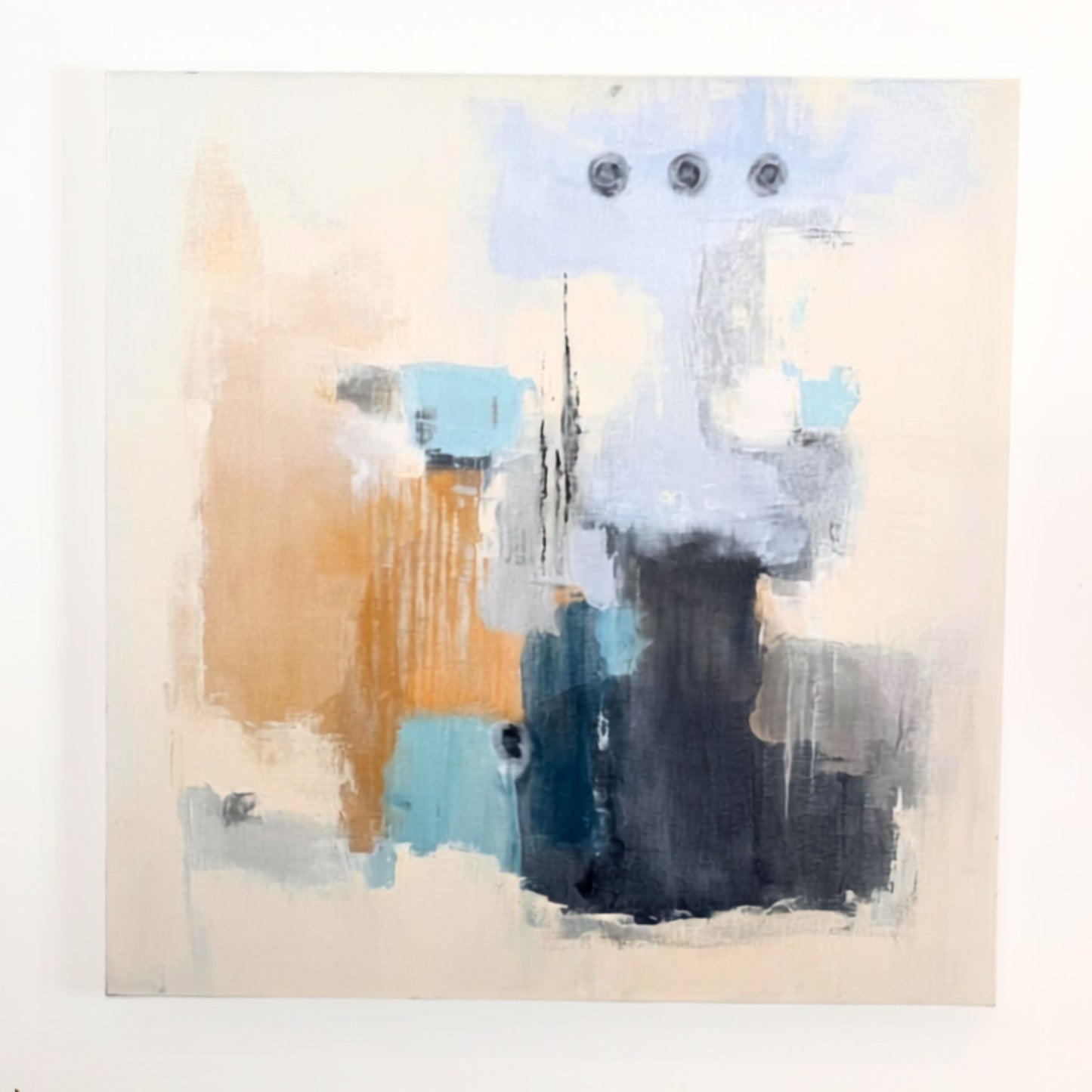 An abstract canvas painting featuring a mix of light blue, dark charcoal, teal, and warm tan brushstrokes on a cream background, with three small circular details near the top.