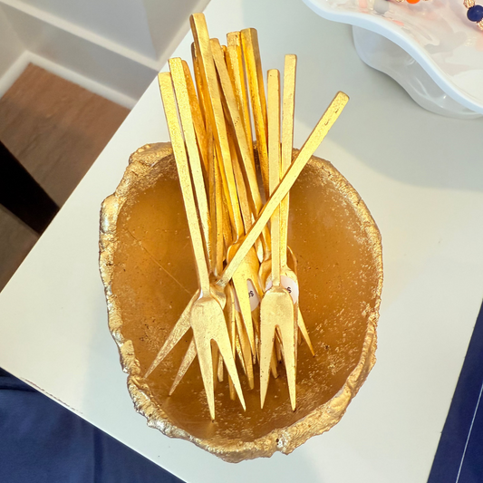Gold forks in a decorative holder on a white surface