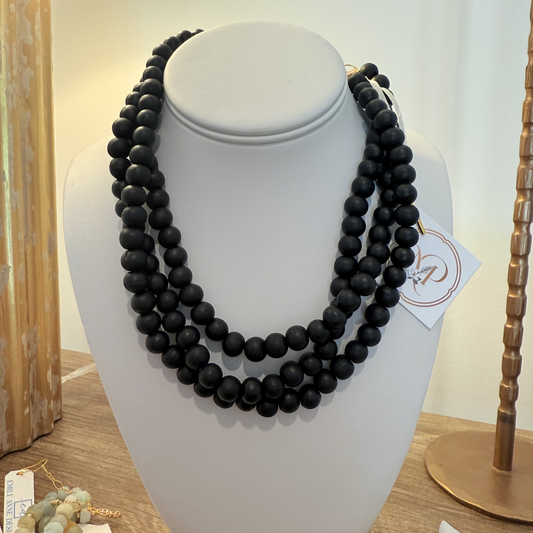 A multi-strand black beaded necklace displayed on a white jewelry bust, with a small paper tag attached near the right side.