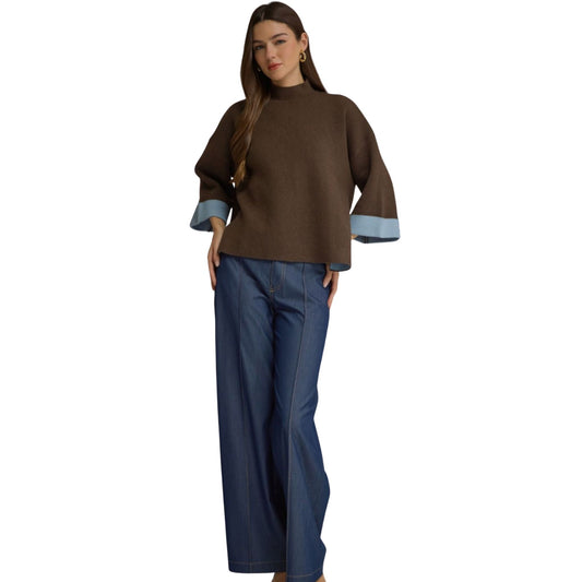 A woman wearing a brown swing sweater top with blue contrast cuffs, paired with dark wash wide-leg jeans.