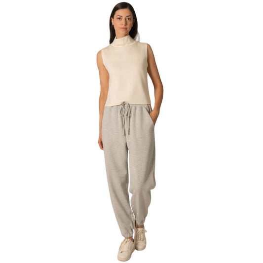 A woman wearing an ivory sleeveless cowl-neck top with gray joggers.