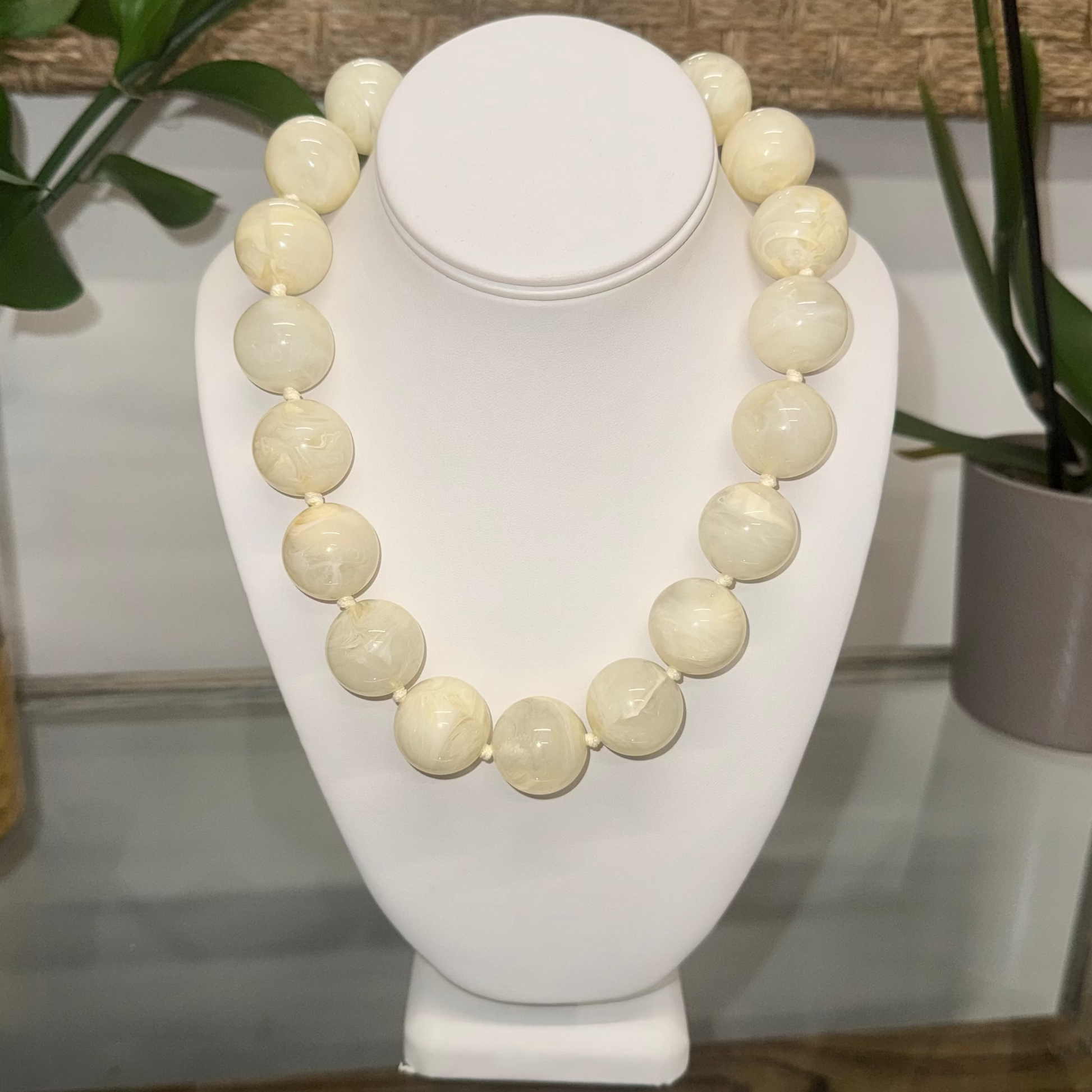 White beaded necklace on a white bust with plants in the background