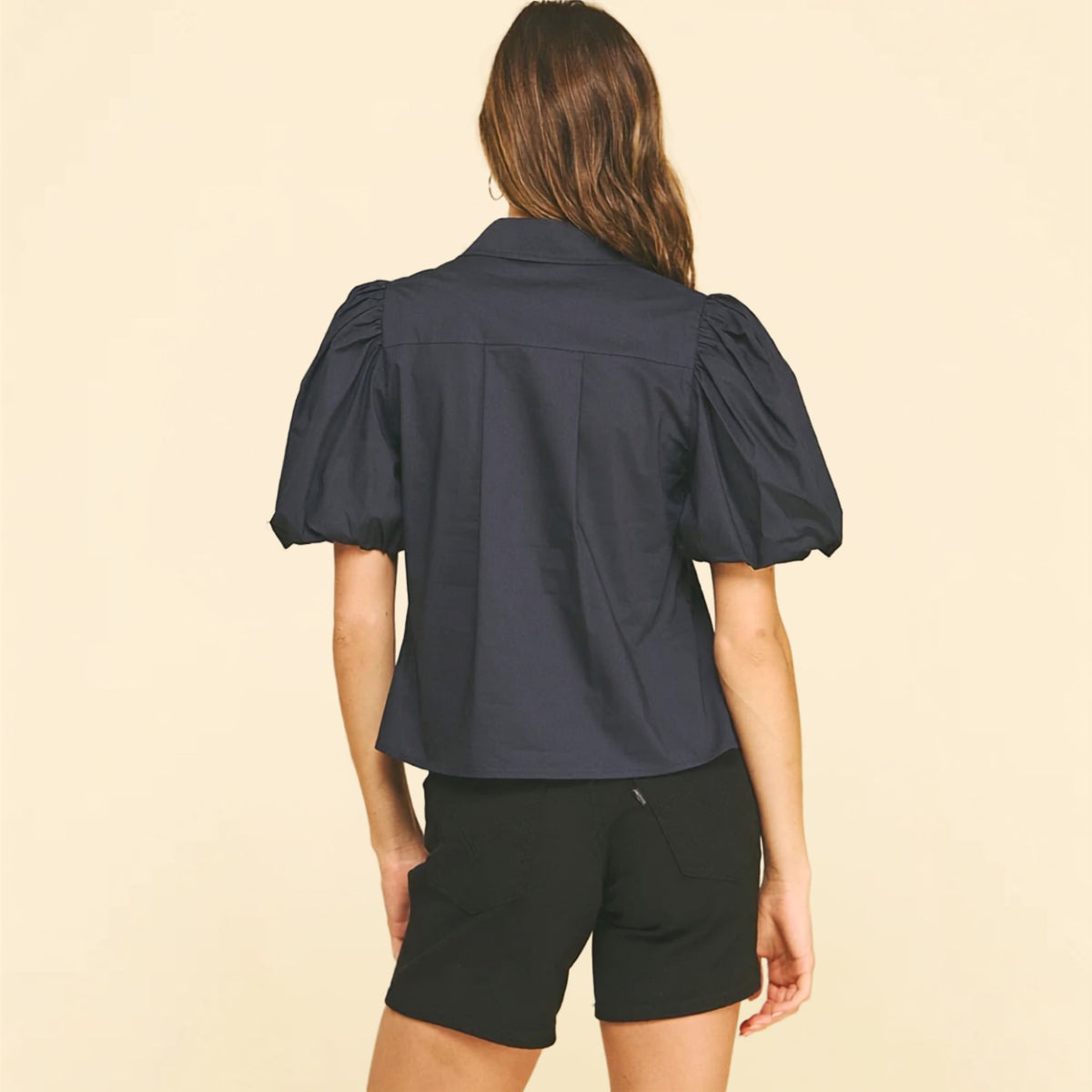 Back view of a black blouse with dramatic puff sleeves and a V-neckline.