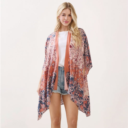 A model wearing an open-front paisley-floral print kimono in navy, terracotta, and cream over a white top and denim shorts.