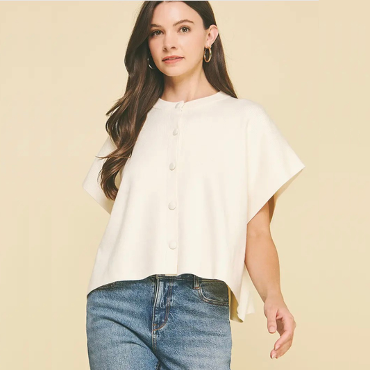 A woman wearing a short-sleeve cream-colored button-front top and blue jeans, standing against a solid light beige background.