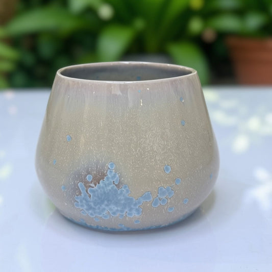 Chubby handmade ceramic cup with speckled greige glaze and crystalline blue bloom near the base