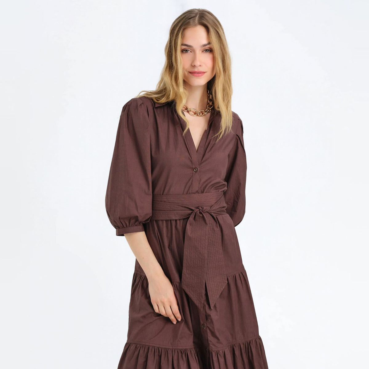 Woman wearing a cocoa brown tiered maxi shirtdress with a tie waist and puff sleeves