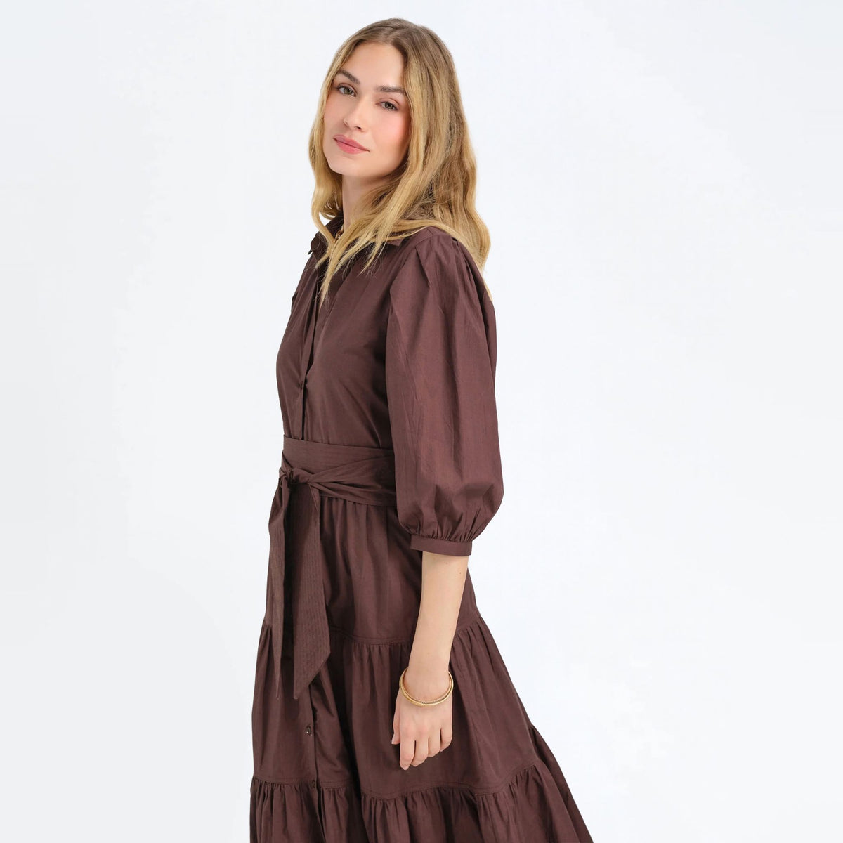 Side view of a woman wearing a cocoa brown tiered maxi shirtdress with puff sleeves