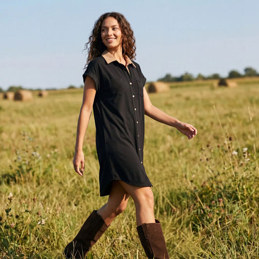 Woman in a black short-sleeve suede shirt dress and boots standing in a hay field