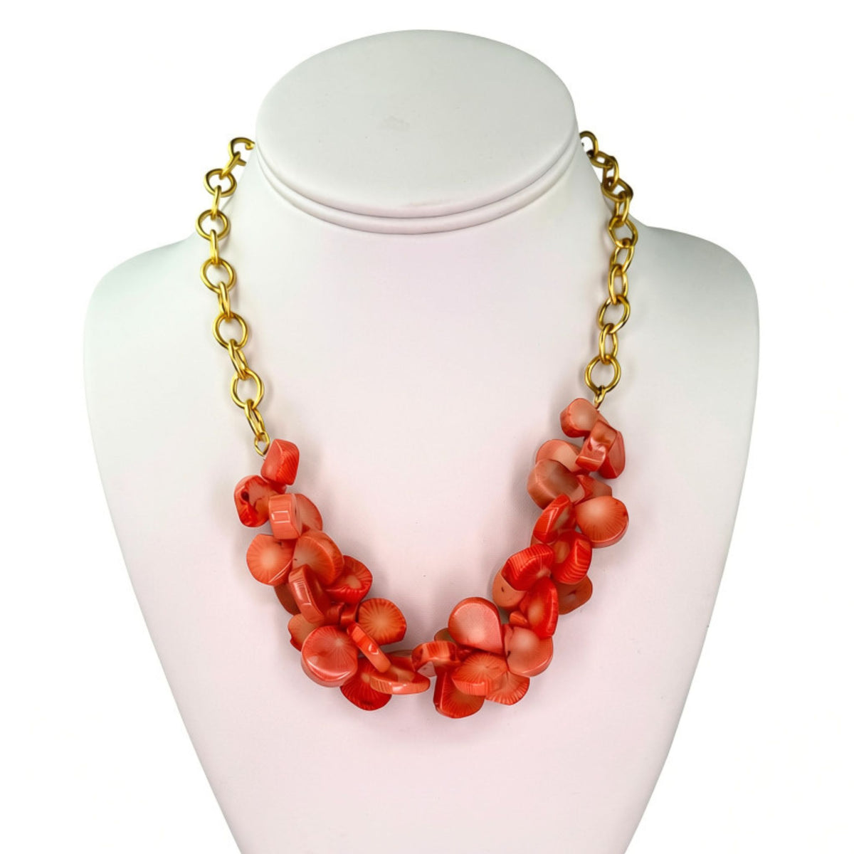 A coral-orange shell bead statement necklace with a gold chain, displayed on a white mannequin bust against a white background.