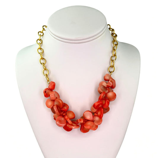 A coral-orange shell bead statement necklace with a gold chain, displayed on a white mannequin bust against a white background.