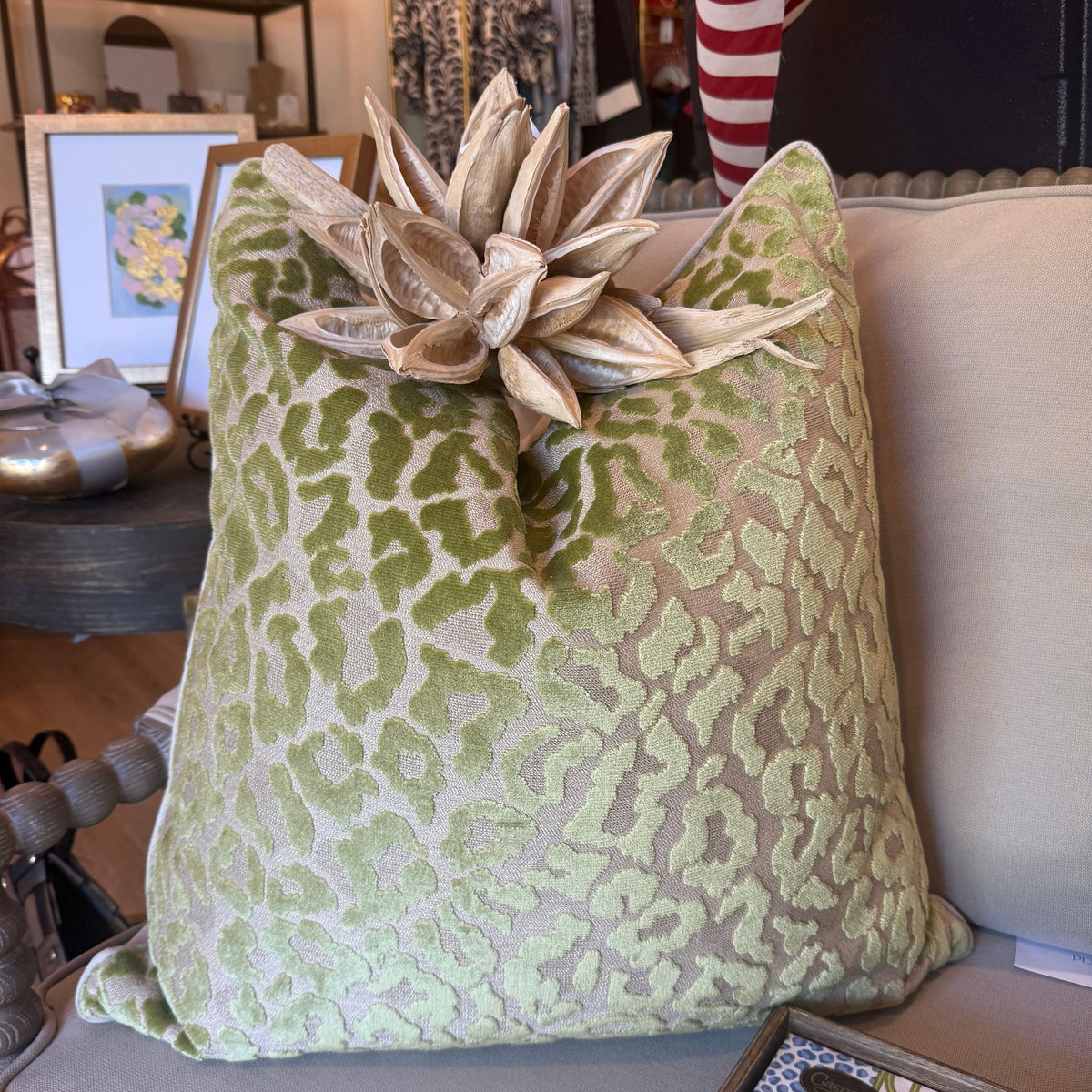A green leopard print cut-velvet pillow styled on a console table among framed art and dried florals.