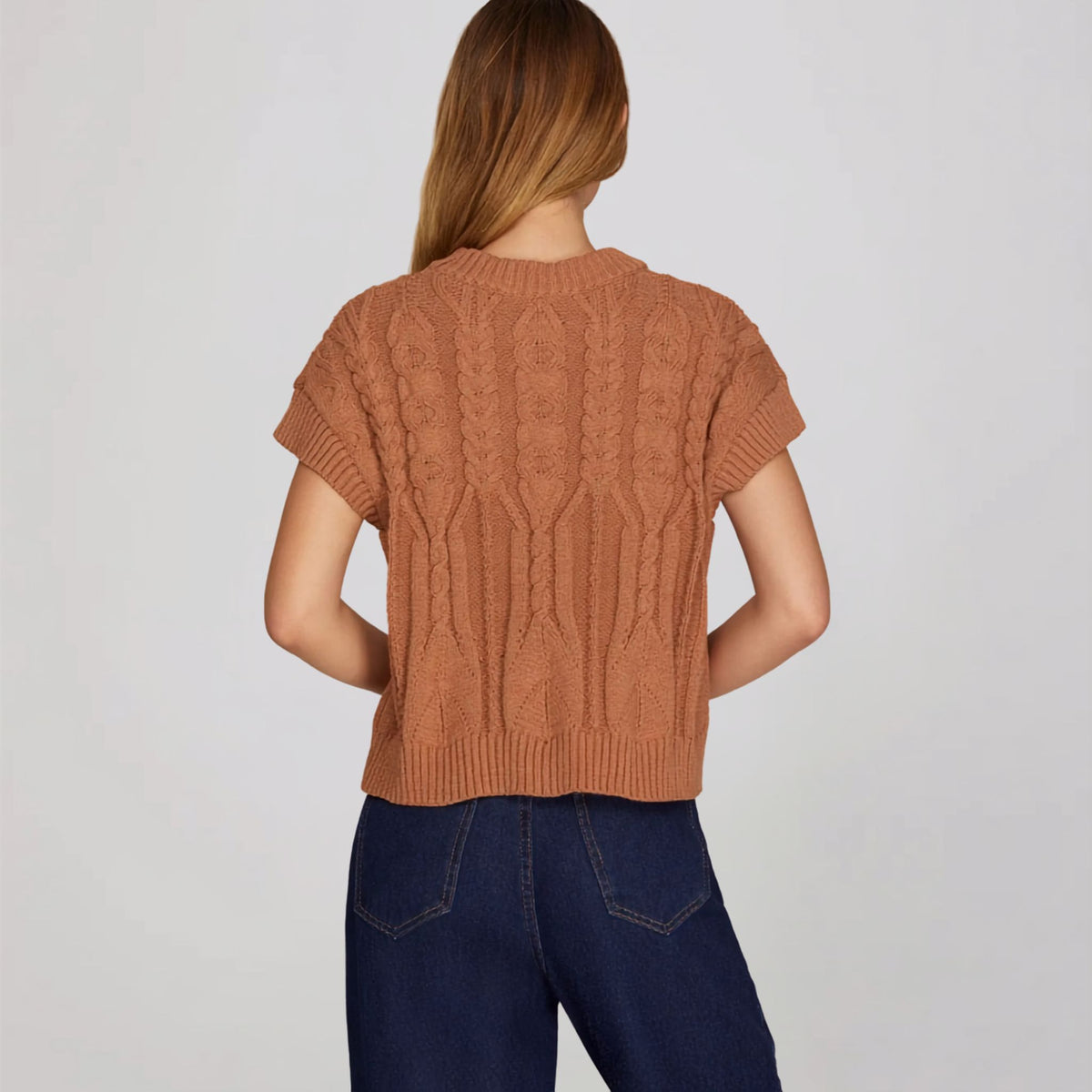 Back view of a cinnamon-colored cable knit sweater with a drop-shoulder fit.