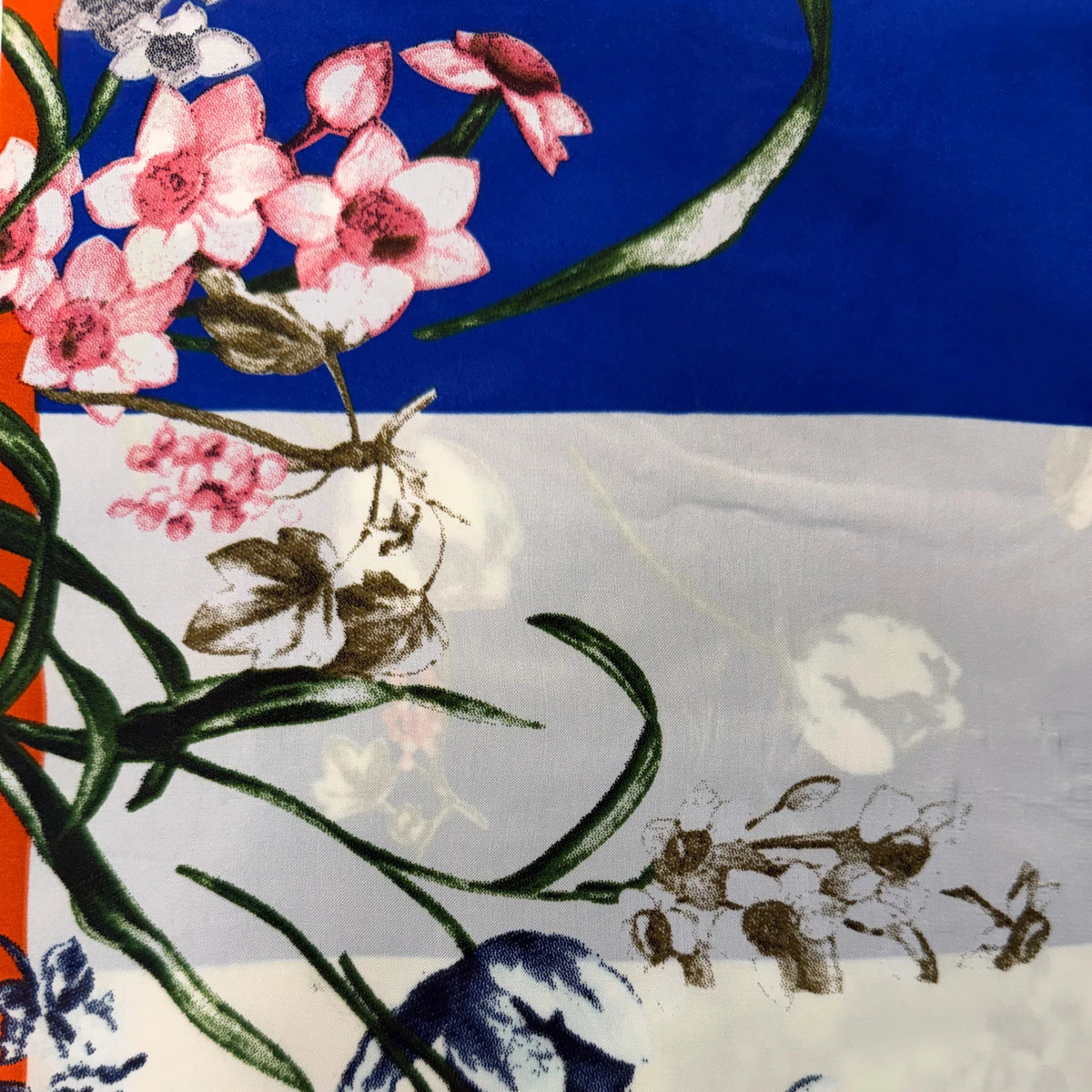 A close-up of a printed scarf featuring pink and white flowers with green leaves over a blue and white striped background.