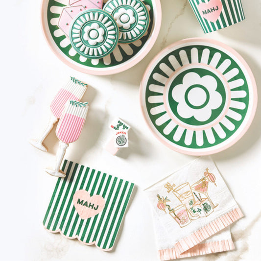 A party table set with green, white, and blush-pink plates, striped cocktail glasses, and matching mahjong-print napkins.