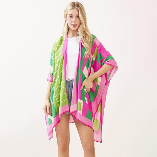 A model wearing an open-front geometric colorblock kimono in pink, green, and cream over a white top and denim shorts.