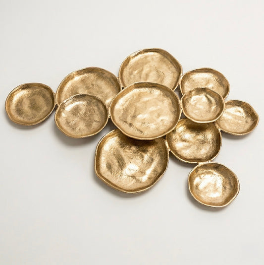 A set of hammered gold metallic dishware pieces, including shallow bowls and small plates, arranged on a plain light background.
