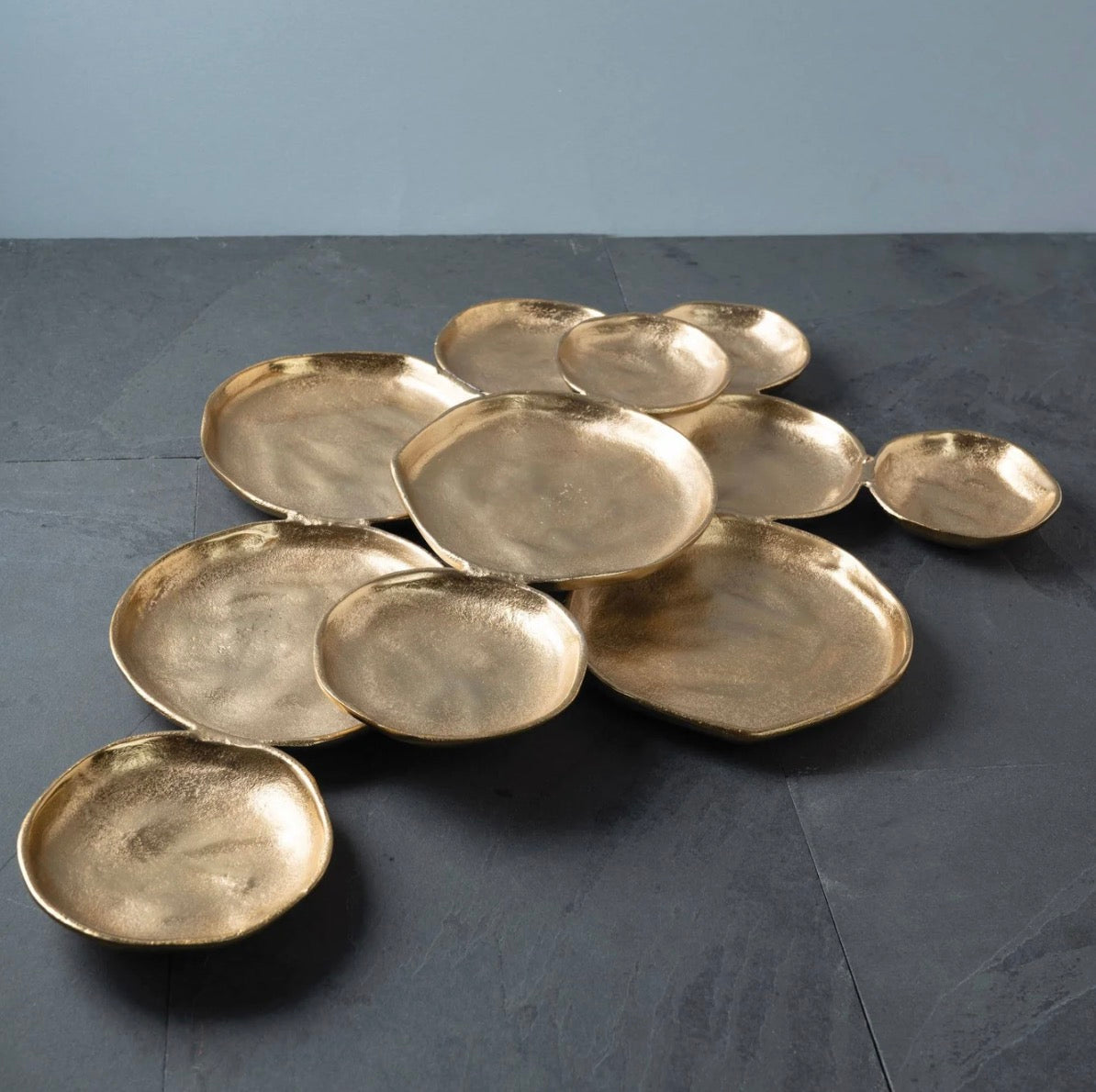 A set of organic-shaped gold ceramic plates arranged on a dark slate surface against a light gray background.