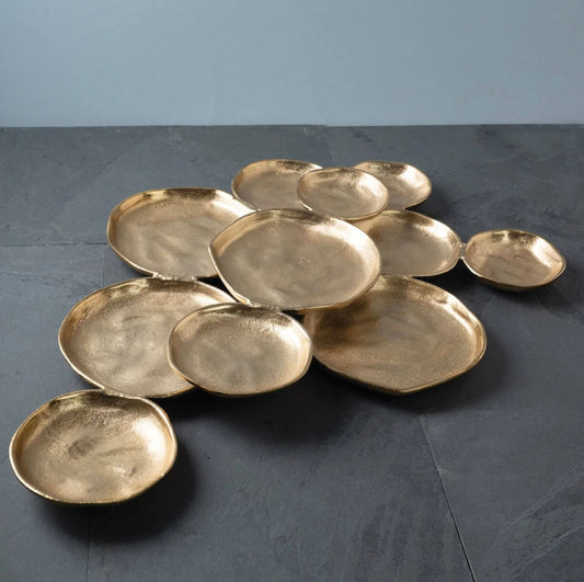 A set of organic-shaped gold ceramic plates arranged on a dark slate surface against a light gray background.