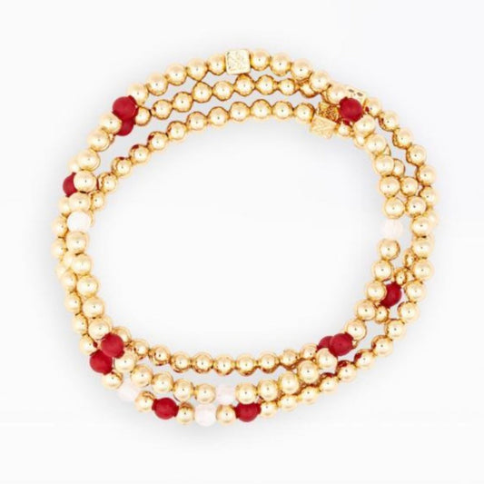 A multi-strand beaded bracelet featuring textured gold beads, deep red faceted beads, and small white beads, arranged in a circular loop on a plain white background.