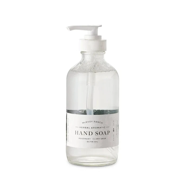 A clear glass pump bottle of hand soap with a white dispenser and a white label reading 'Hand Soap' on a plain white background.