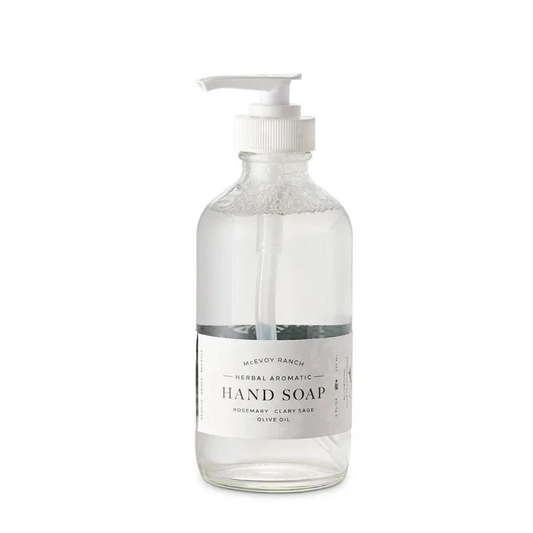A clear glass pump bottle of hand soap with a white dispenser and a white label reading 'Hand Soap' on a plain white background.