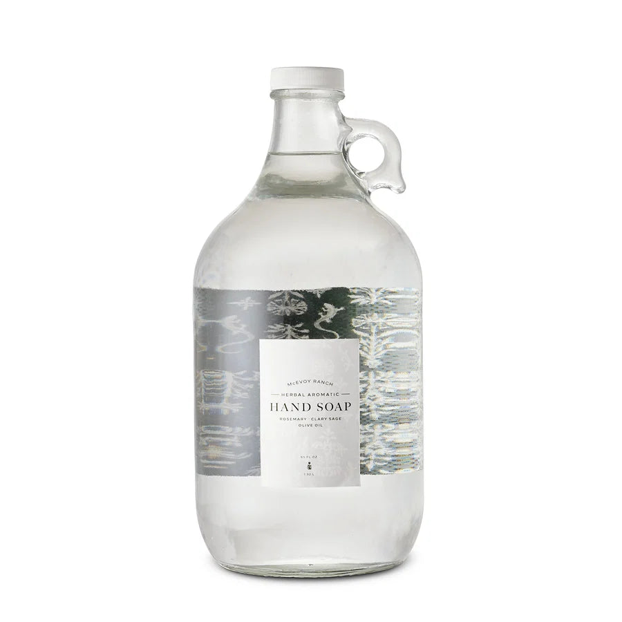 A clear glass growler bottle of hand soap with a white cap and a central label reading 'Hand Soap' on a white background.