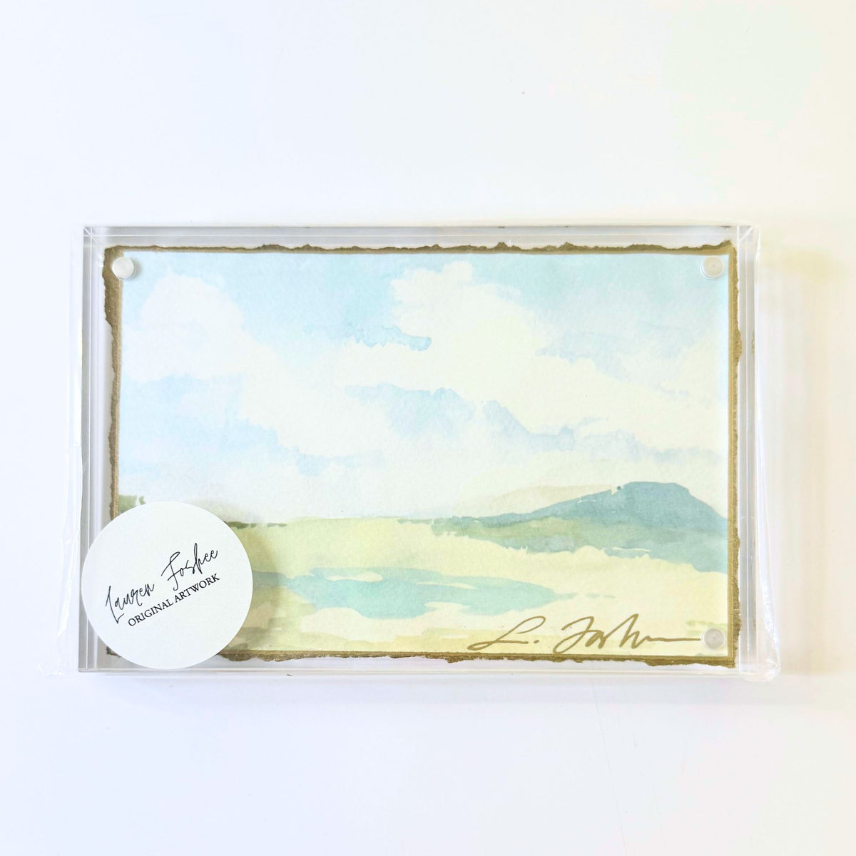 Lauren Foshee signed watercolor print, sky and clouds over a soft blue mountain and pale marsh, in a clear acrylic floating frame