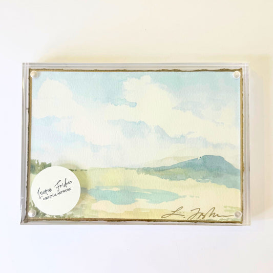 Lauren Foshee signed watercolor print, sky and clouds over a soft blue mountain and pale marsh, in a clear acrylic floating frame