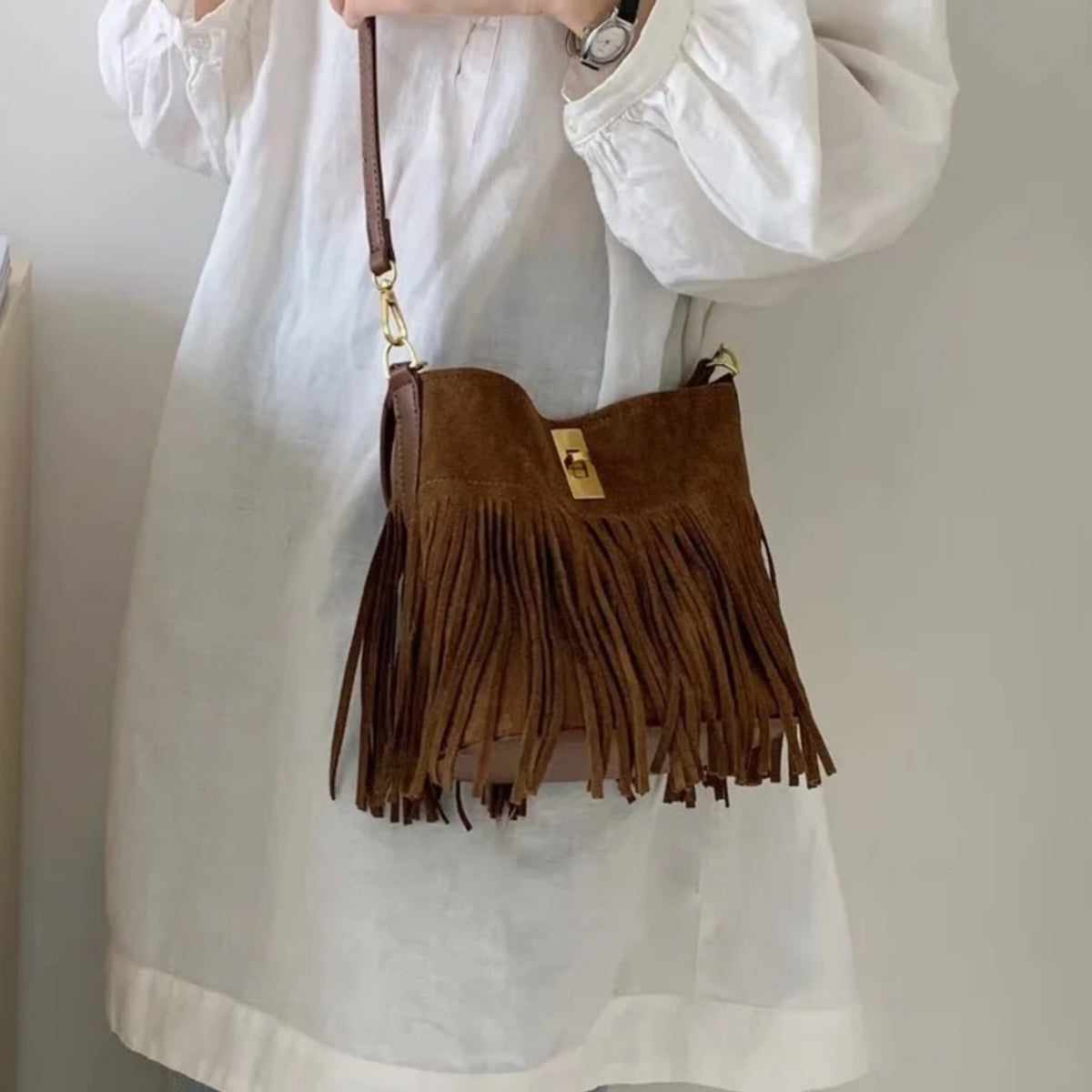 Woman wearing a brown suede fringe bucket bag across her body
