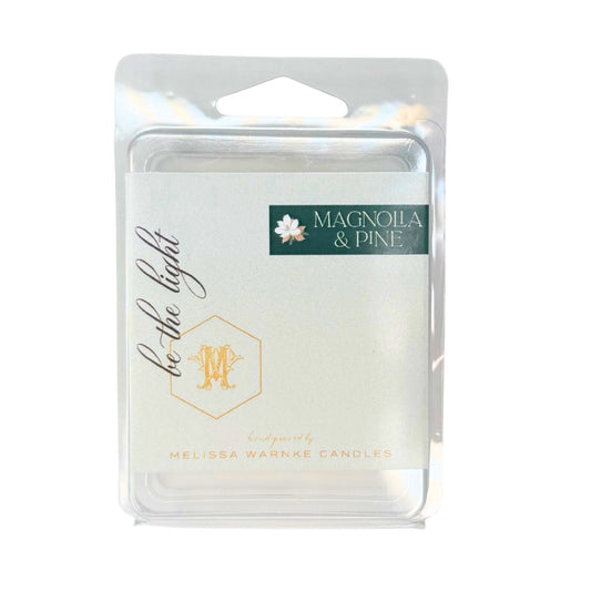 A packaged wax melt or scented melt product in a clear plastic clamshell package with a white label. The label reads 'MAGNOILA & PINE' and 'be-the-light' with a gold monogram, and 'Made by Melissa Wannek Candles' appears at the bottom.