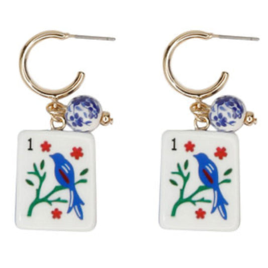 A pair of gold hoop earrings with a blue-and-white patterned bead and a white mahjong tile marked 1, showing a blue bird on a branch with red flowers.