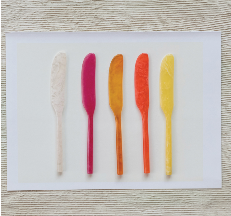 Five colorful butter knives on a white card with a wooden surface background