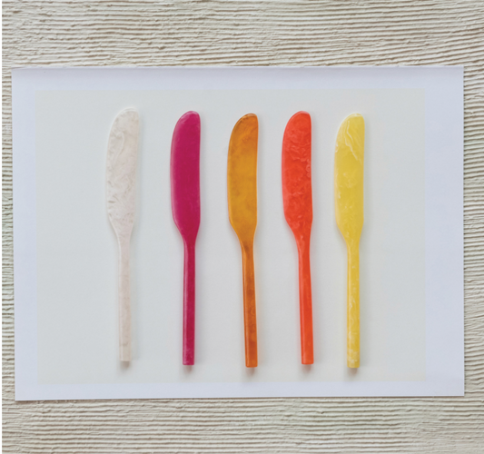 Five colorful butter knives on a white card with a wooden surface background