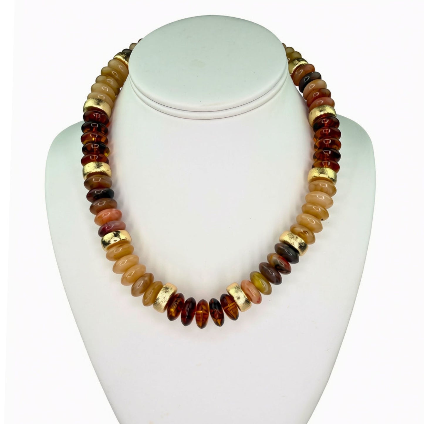 A beaded necklace displayed on a white mannequin bust, featuring polished round beads in amber brown, golden yellow, and terracotta tones with metallic gold spacer accents.
