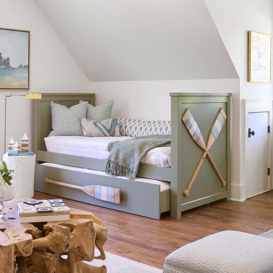 A sage-green Twin XL trundle bed with an oar-inspired pull-out design, styled with pillows and a throw blanket.