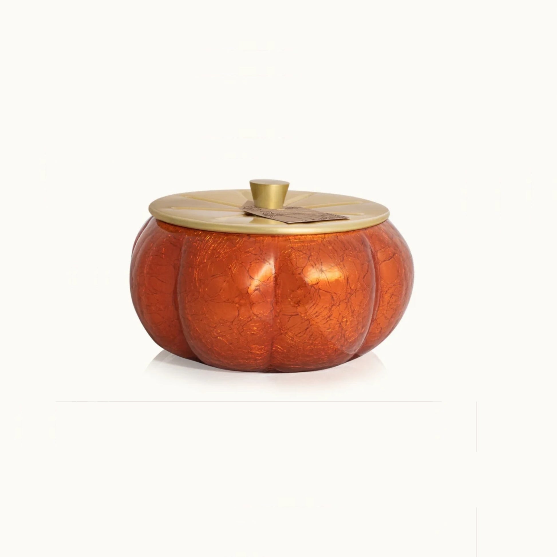 A decorative pumpkin-shaped candle with a glossy orange body and a round gold lid, shown on a clean white background.