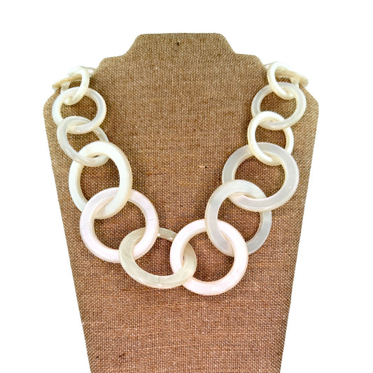 A chunky statement necklace made of large, interlocking circular links in a milky translucent white, displayed on a brown burlap jewelry bust against a white background.