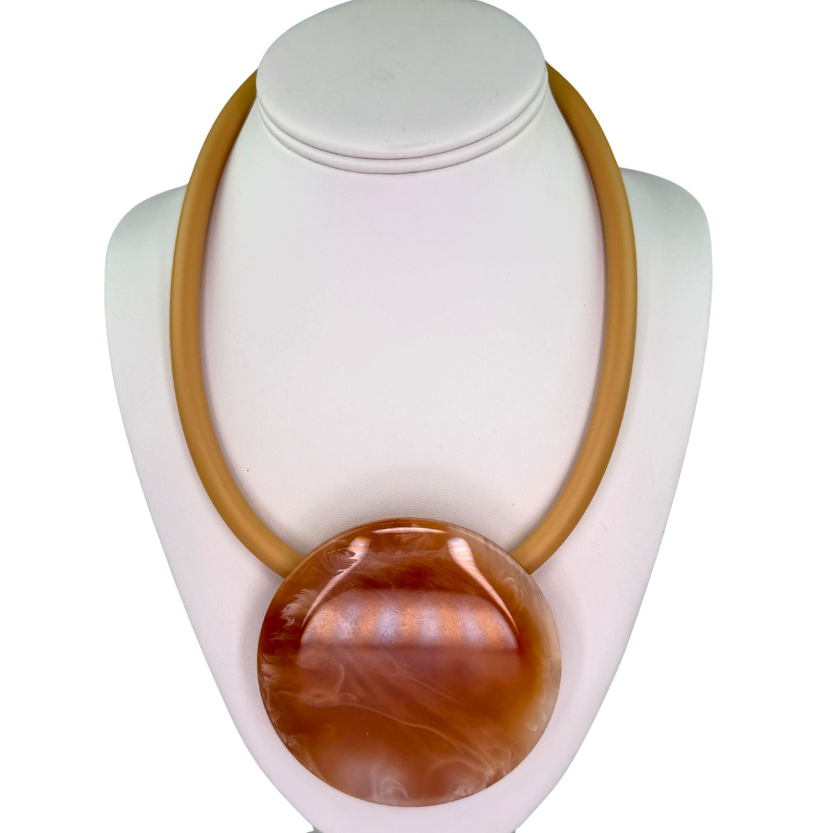 A chunky statement necklace with a large polished oval pendant in warm amber-brown tones, displayed on a white jewelry bust against a white background.