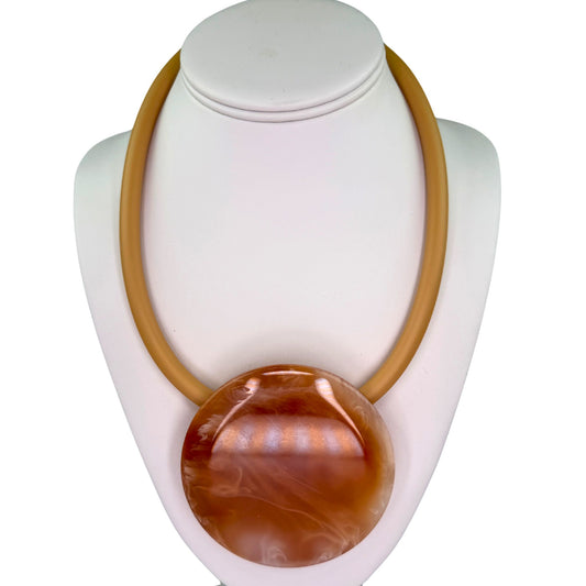 A chunky statement necklace with a large polished oval pendant in warm amber-brown tones, displayed on a white jewelry bust against a white background.