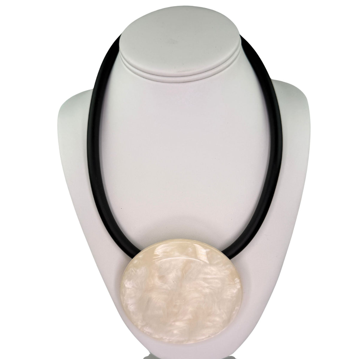 A black cord necklace with a large, round, textured cream-colored shell pendant, displayed on a white jewelry bust against a white background.