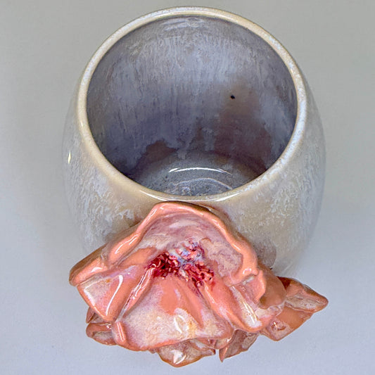 A ceramic vase viewed from above, showing a lavender-gray glazed interior and a sculpted, glossy pink flower bloom with a red center attached near the base.