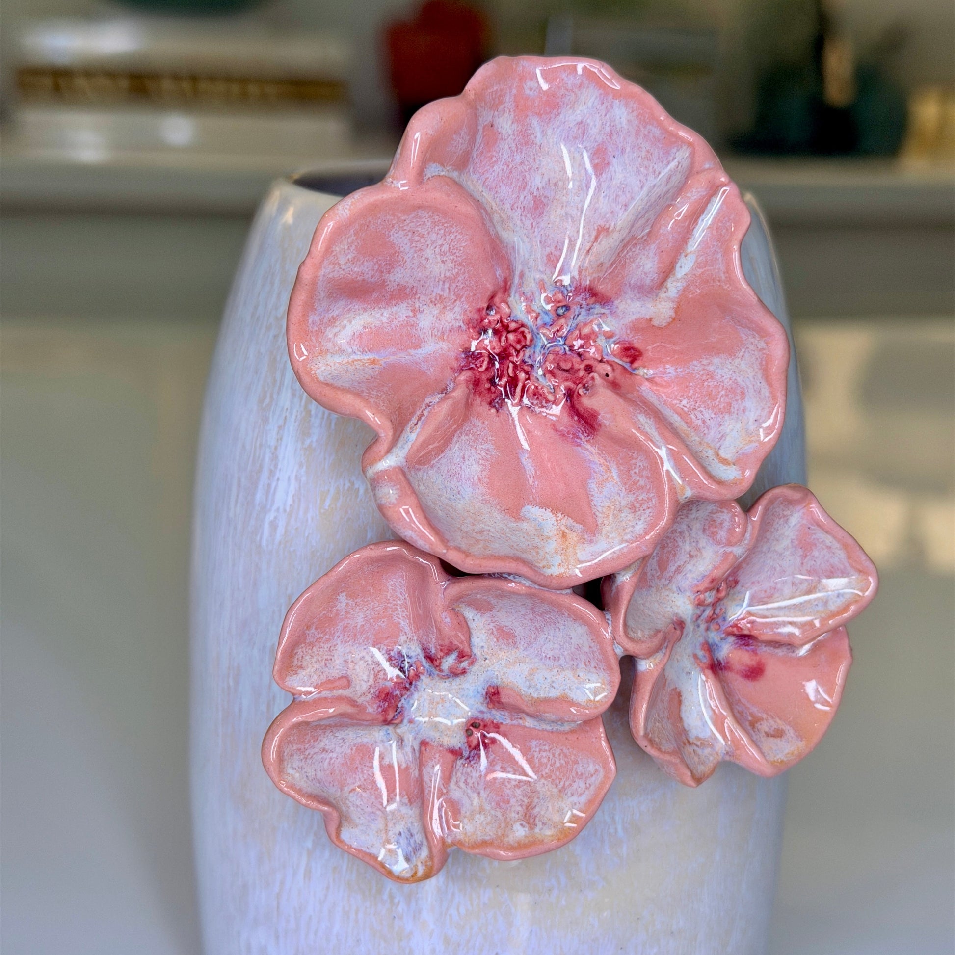 A close-up of a ceramic vase's textured grey-white glaze and three raised pink flower blooms with red centers.