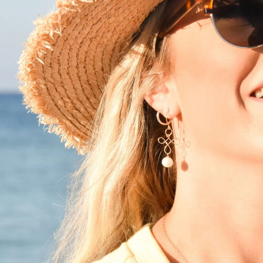 Woman wearing a straw hat, pearl drop earrings and sunglasses with a blurred background