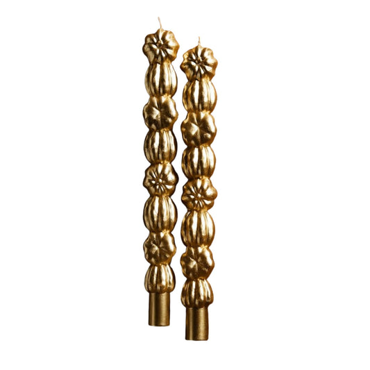 Two tall gold taper candles with a textured, stacked pumpkin design, shown against a plain white background.