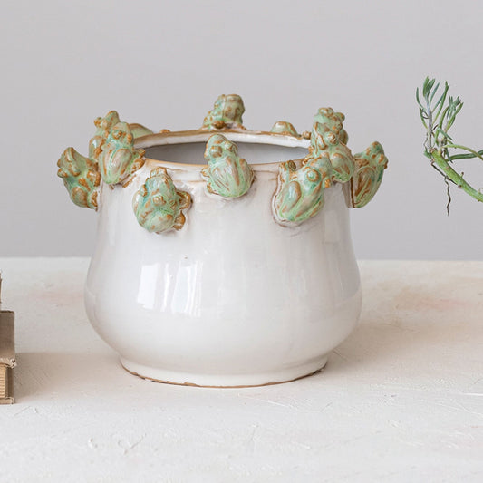 Decorative ceramic pot with green frog accents on a white surface.