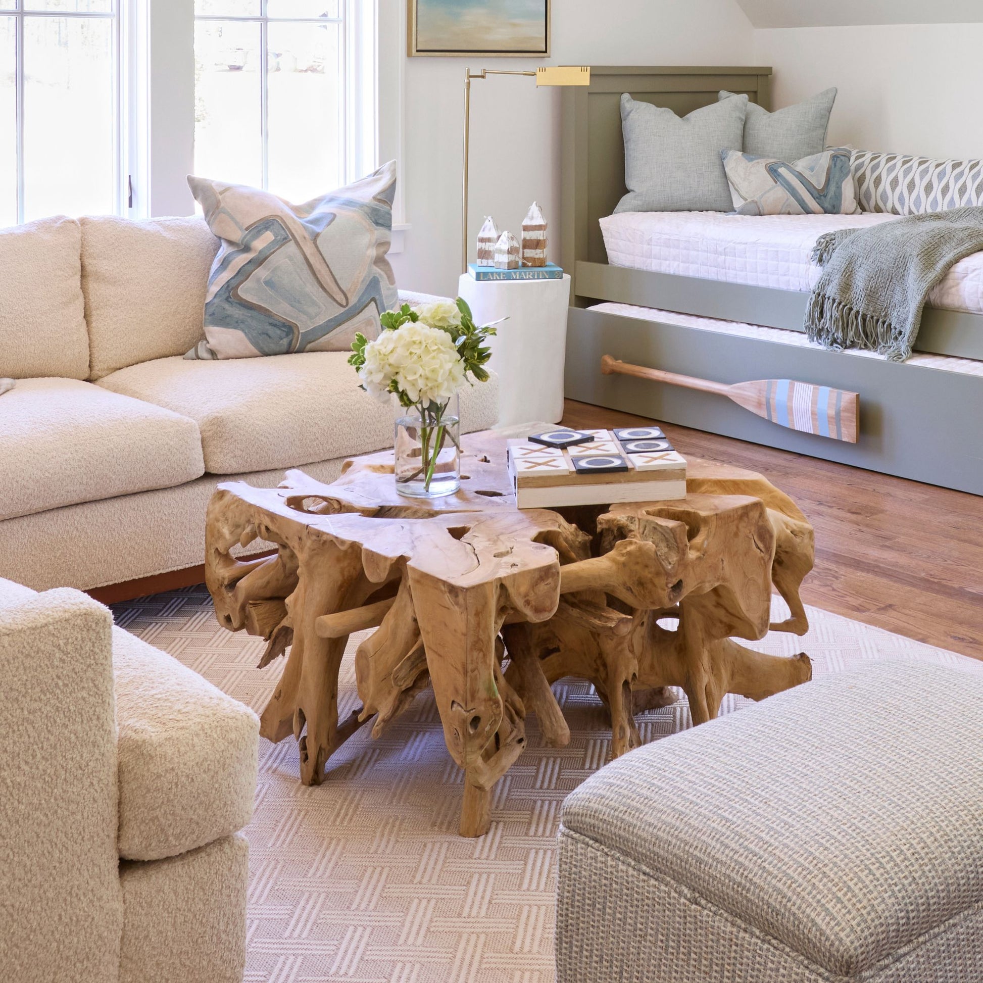 A teak coffee table with a sculptural, raw teak root base and a smooth teak slab top, styled in a lake house living room.