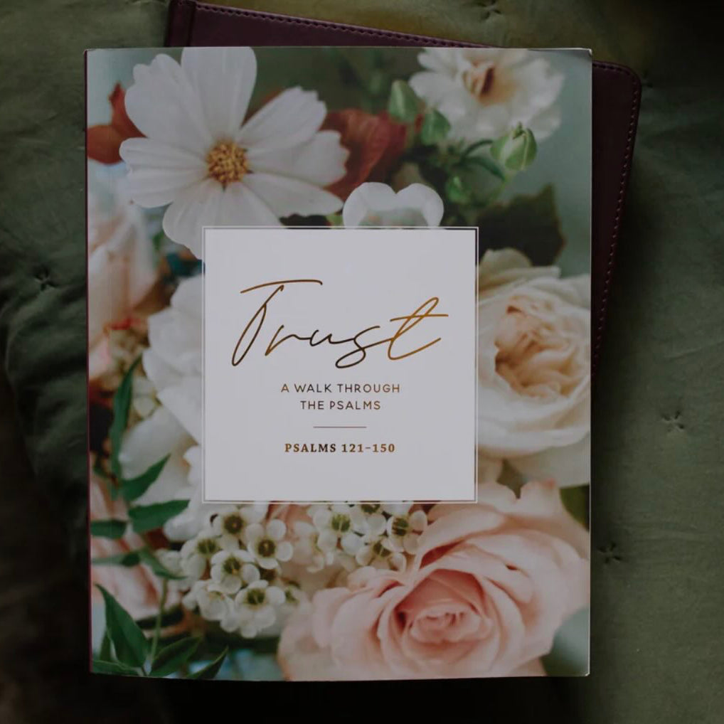 A book titled 'Trust: A Walk Through The Psalms' featuring a floral cover with white and pink flowers, set against a dark green textured fabric background.