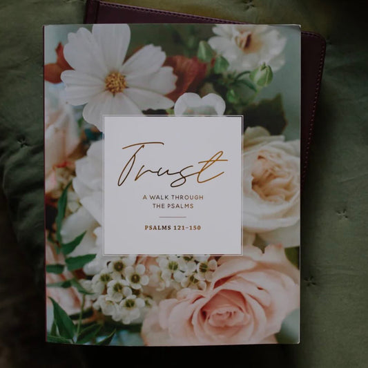 A book titled 'Trust: A Walk Through The Psalms' featuring a floral cover with white and pink flowers, set against a dark green textured fabric background.